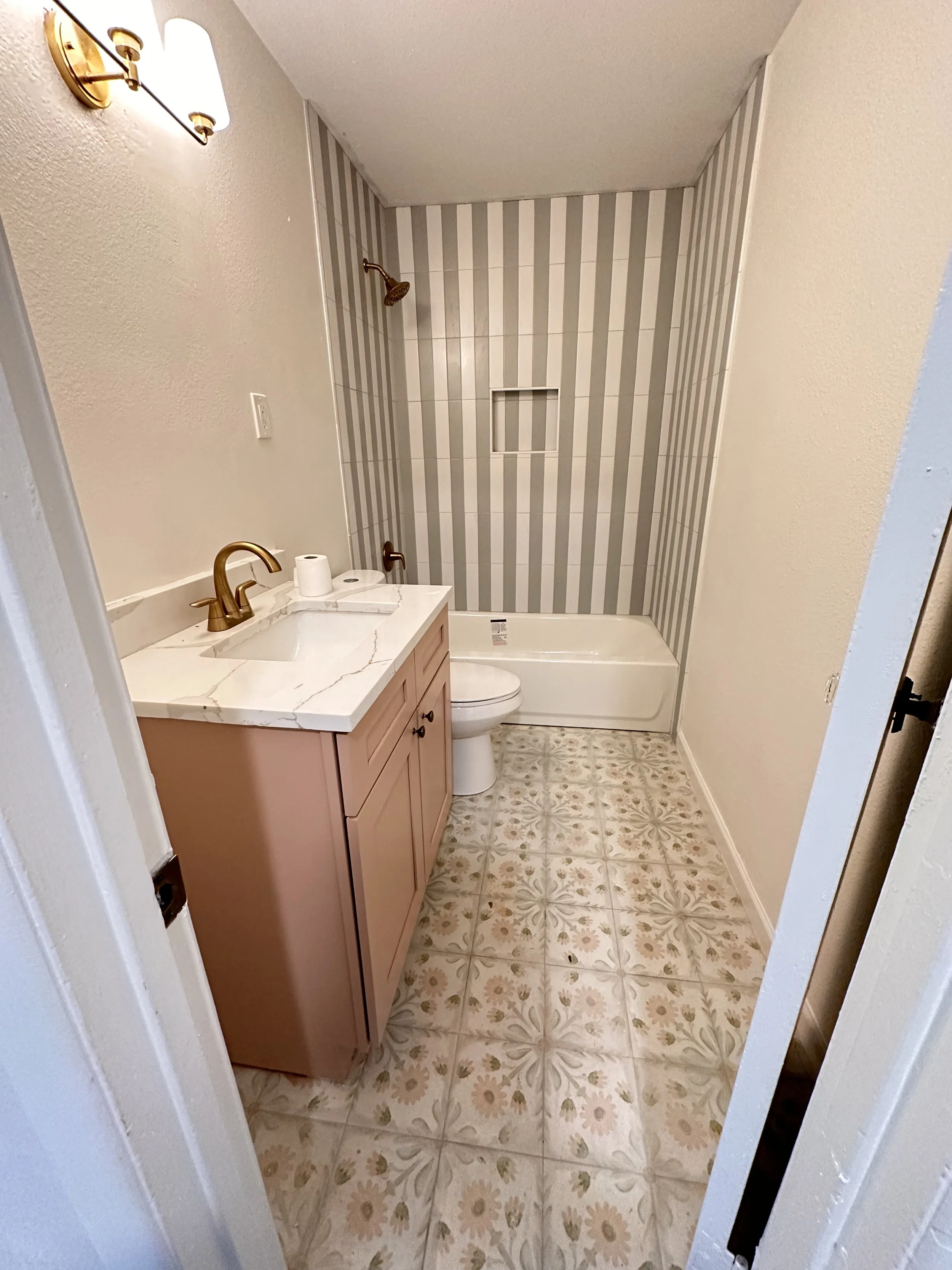 Bathroom with pink vanity, marble countertop and striped tile